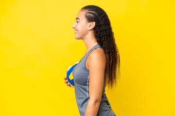 Wall Mural - Young woman playing volleyball isolated on yellow background laughing in lateral position