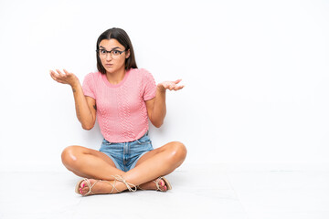 Wall Mural - Young caucasian woman sitting on the floor isolated on white background having doubts while raising hands