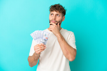 Canvas Print - Young caucasian man taking a lot of money isolated on blue background and looking up