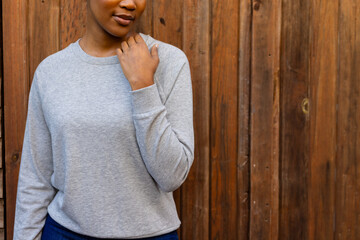 Wall Mural - Midsection of african american woman wearing grey sweatshirt against wooden fence, copy space