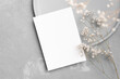 Wedding invitation card mockup with dry gypsophila flowers decor on grey background, top view with copy space