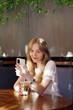 © Dana - beauty blond woman, wearing white t-shirt, sitting in cafe, drinking ice coffee and looking in mobile phone
