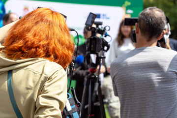 Wall Mural - Red hair female camerawoman filming media event or press conference with a video or television camera. Public relations - PR concept.