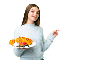 Wall Mural - Teenager girl holding waffles over isolated chroma key background pointing finger to the side