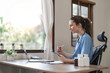 © Natee Meepian - Portrait of cheerful smiling young female doctor in blue medical uniform typing on laptop computer, sitting at desk near window in modern office of medic clinic