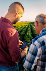 Two farmers standing in a field examining soy crop while using table