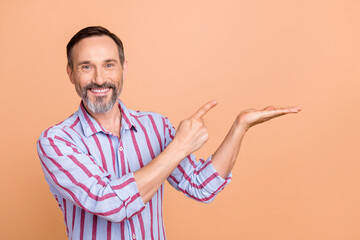 Poster - Photo of positive corporate manager toothy smile indicate finger arm palm hold demonstrate empty space isolated on beige color background