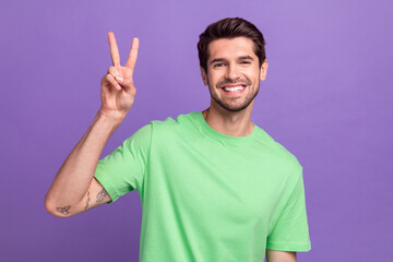 Poster - Portrait of positive good mood nice guy with bristle wear green t-shirt showing v-sign say hello isolated on violet color background