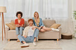 © LIGHTFIELD STUDIOS - love triangle concept, diversity in relationships and culture, non monogamy, happy redhead man and multicultural women looking at camera in living room, lovers, acceptance, open relationship