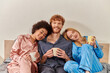 © LIGHTFIELD STUDIOS - open relationship concept, polygamy, redhead man and multicultural women in pajamas holding cups of coffee, morning routine, bisexual, understanding, three adults, cultural diversity, acceptance