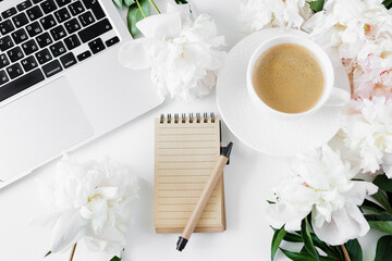 Top view of coffee cup, notebook, pen, laptop and pionies