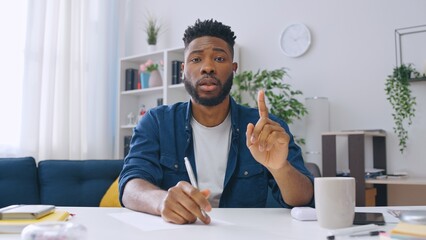 Male student in headphones asking questions and taking notes during online lesson with a teacher