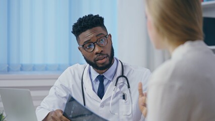 Wall Mural - African American traumatologist consulting female patient after checking her x-ray image