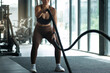 Strong woman doing battle rope exercise at gym, make the rope move in waves for fat burning workout