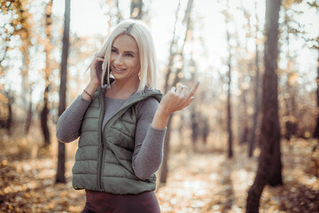 Wall Mural - Smiling fitness blonde woman talking on the phone in autumn forest