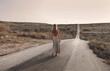 © olly - seen from behind, young woman walks on a deserted road
