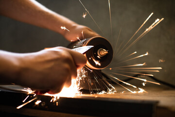 Close-up of men's hands sharpening an axe on an electric sharpener. Repair of home tools. 
Sparks fly.