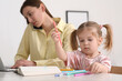 © New Africa - Woman with laptop working remotely at home. Busy mother talking on phone while her daughter drawing at desk. Selective focus