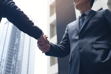 Wall Mural - Asian businessmen making handshake with office building as background,  business etiquette, congratulation, merger and acquisition, business meeting and partnership concepts