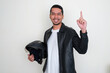 © KrishnaTedjo - Adult Asian man smiling and pointing finger up while holding a motorcyle helmet