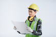 © Kanyanat - Young asian engineer in light green protective suit wearing yellow hat wearing white gloves yellow headphones holding document happy gesture checking work white background design