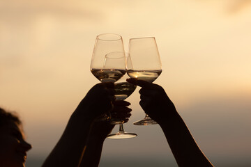 Wall Mural - Group of friends with white wine in hands clinking with glasses. Close-up of hands and drinks. Beautiful scenic sunset.	