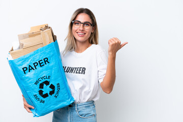 Canvas Print - Young pretty Uruguayan woman holding a recycling bag full of paper to recycle isolated on white chroma background pointing to the side to present a product