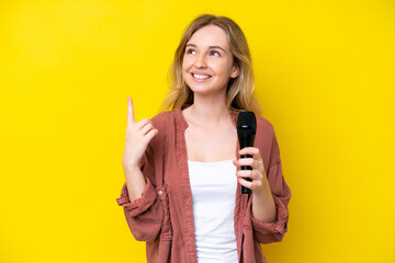 Young singer caucasian woman picking up a microphone isolated on yellow background pointing up a great idea