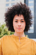 © Jose Calsina - Vertical individual portrait of young adult woman looking pensive at camera standing outside. Head shot of proud hispanic female with serious expression and curly hair. Successful lady contemplating