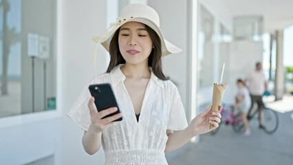 Sticker - Young chinese woman tourist eating ice cream using smartphone at street