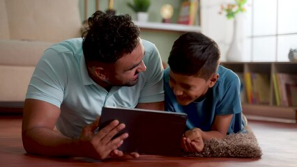 Wall Mural - joyful indian father with son using digital tablet while lying on floor at home - concept of weekend holiday, Modern parenting and Digital entertainment