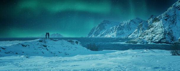 Fototapete - Couple travelers Man and Woman stand and enjoy the impressively beautiful northern lights over North fjord and rocky mountains in winter, Lofoten islands. Norway. Travel adventure Lifestyle concept