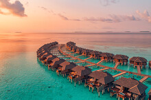 Sunset On Maldives Island, Luxury Water Villas Resort And Wooden Pier. Beautiful Aerial Sky Clouds And Beach Background. Summer Coast Vacation Travel. Paradise Sunrise Landscape. Pristine Sea Bay