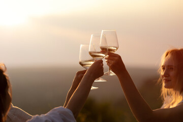 Wall Mural - Friends holding glasses of wine at sunset. Chin-chin. Copy space.