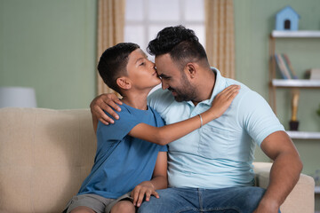 Wall Mural - Happy indian son kissing his fathers forehead while sitting on sofa at home - concept of affection, Family love and tender moment.