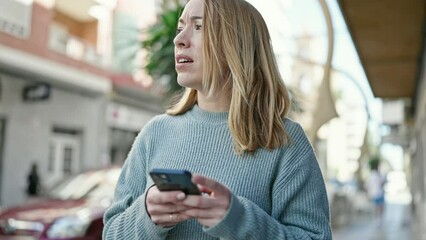 Poster - Young blonde woman using smartphone with serious expression at street