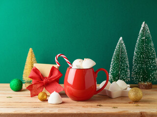 Wall Mural - Christmas hot chocolate cup with marshmallow, gift box and decorations on wooden table over green background. Festive greeting card