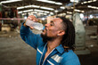 © KANGWANS - African male worker drinking water and resting after working in industrial factory.