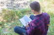 A man is reading a book in the park. Reading a book outdoors. Outdoor recreation