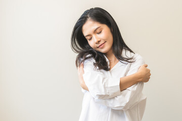 Wall Mural - Smiling positive, hugging oneself happy asian young woman hands hug herself shoulders enjoy joyful, self hugging, self love and self care, face expression self esteem standing isolated on background.