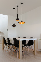 dining room with white and wood table and six black chairs with three black metal lamps hanging from