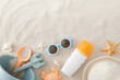 Sun care for children's delicate skin. Top view composition of UV-protection spray, eyewear, beach toys, panama hat, seashells, starfish on sand background with empty space for promo or text