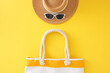 Beach retreat idea for the summer. Top view photo of beach handbag, sun hat, eyewear on yellow background
