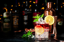 Bramble Alcohol Cocktail Drink With Dry Gin, Liqueur, Syrup, Lemon Juice, Blackberry And Ice. Black Bar Counter Background, Steel Bar Tools And Bottles