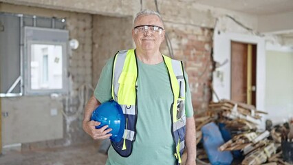 Wall Mural - Middle age grey-haired man builder smiling confident holding hardhat at construction site