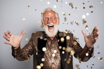 Wall Mural - Portrait of a happy senior man throwing confetti isolated on a gray background