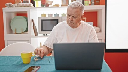 Canvas Print - Middle age grey-haired man using laptop wearing glasses at dinning room