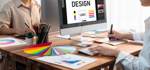 Poster - Graphic designer work on computer laptop and with graphic drawing pen while brainstorming unique design with professional graphic team in modern digital studio workplace. Panorama shot. Scrutinize