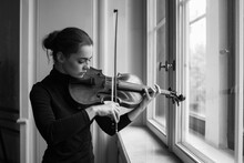 Monochrome Portrait Of Young Woman Playing Violin Near Window