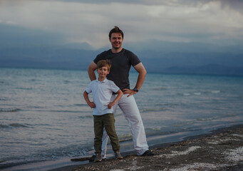 Canvas Print - Happy father and son standing on the lake shore at windy weather